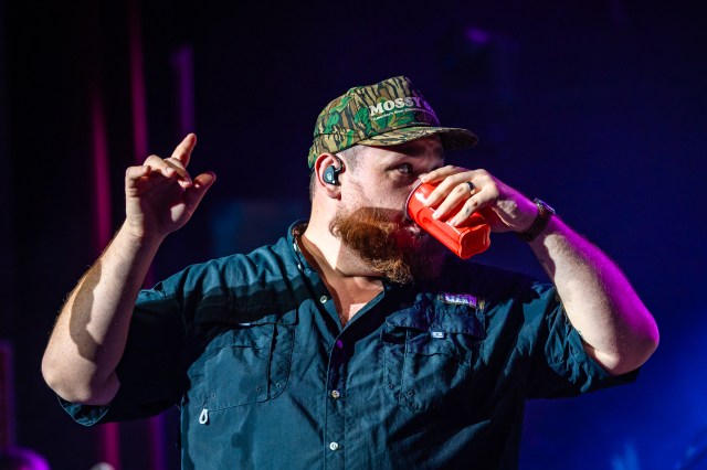 Luke Combs drinks beer from a solo cup on stage.