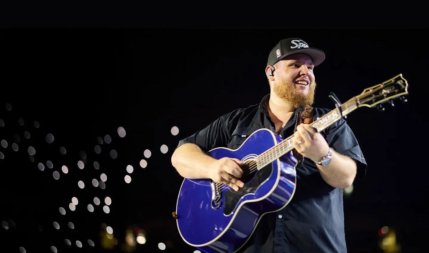 Luke Combs smiling on stage with a guitar
